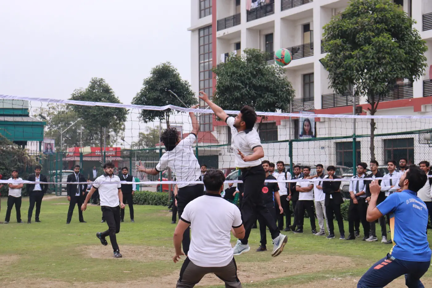 Campus sports ground with volleyball game and buildings behind